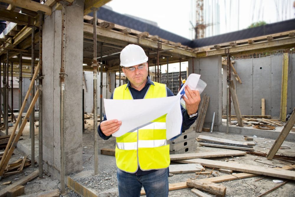 A man in yellow vest holding papers and wearing safety glasses.